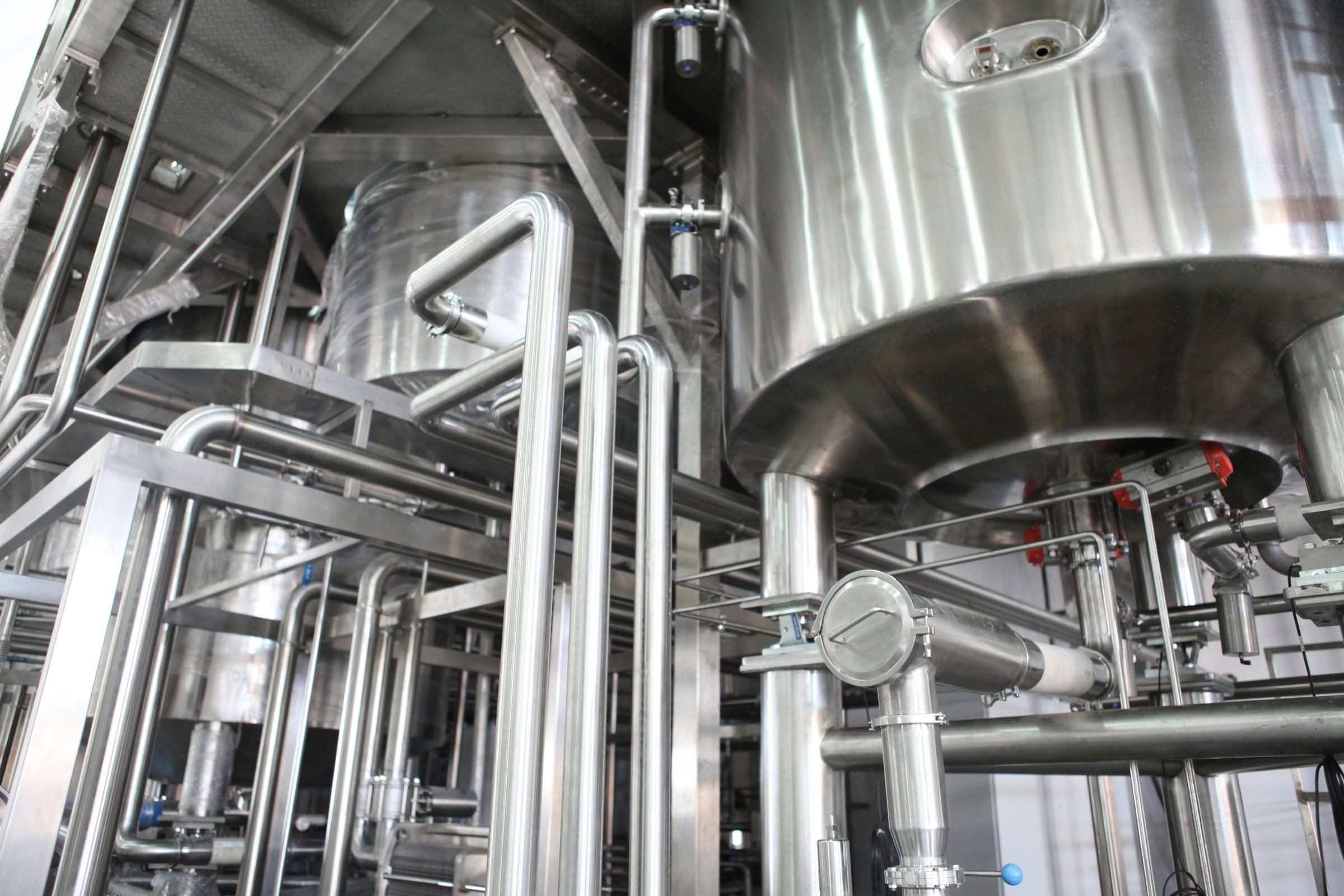 Tanques de proceso y tuberías sanitarias de acero inoxidable en una planta industrial.