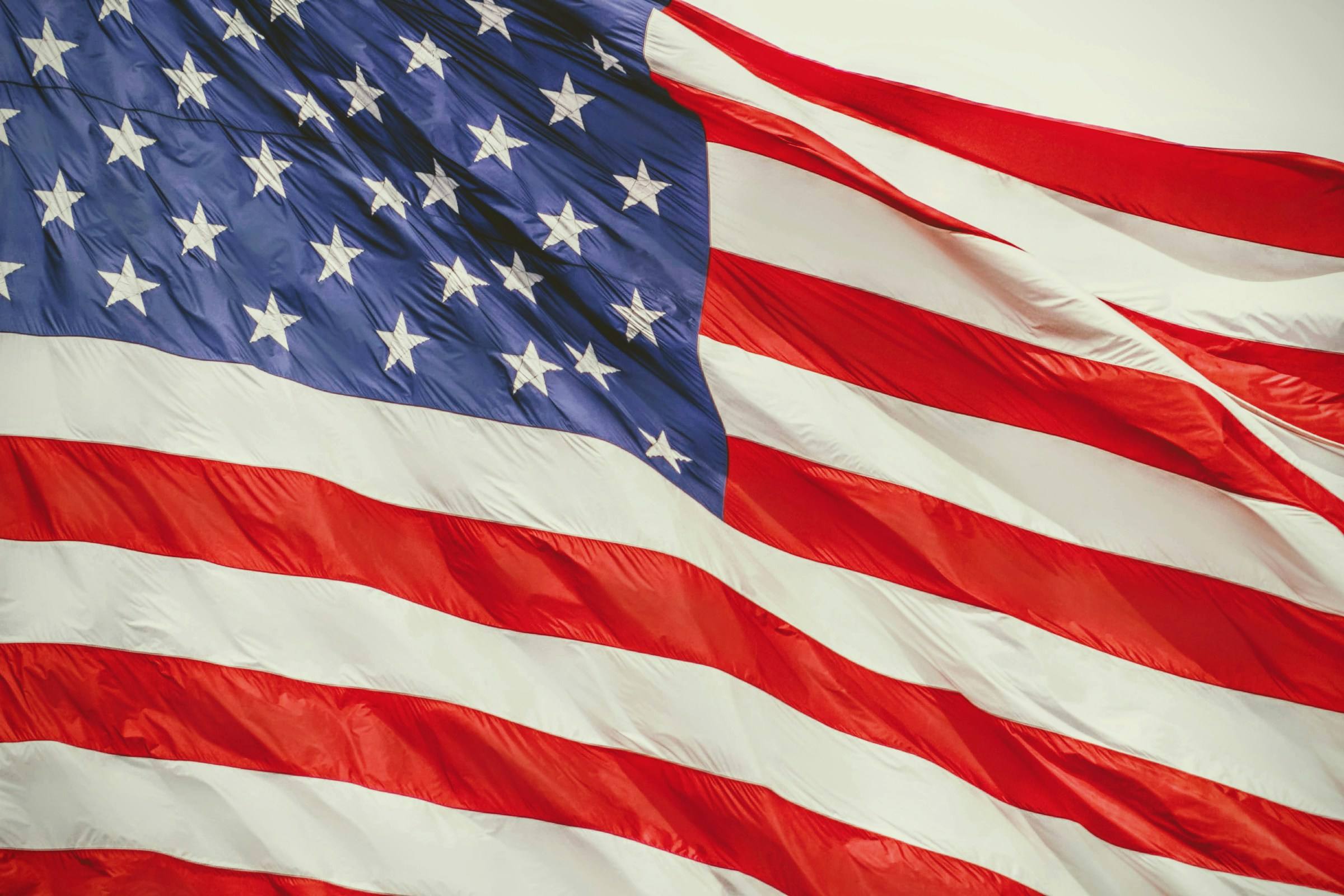 Close-up of a large United States flag rippling in the wind, with white stars on a blue field at upper left and red and white stripes sweeping diagonally across the frame.